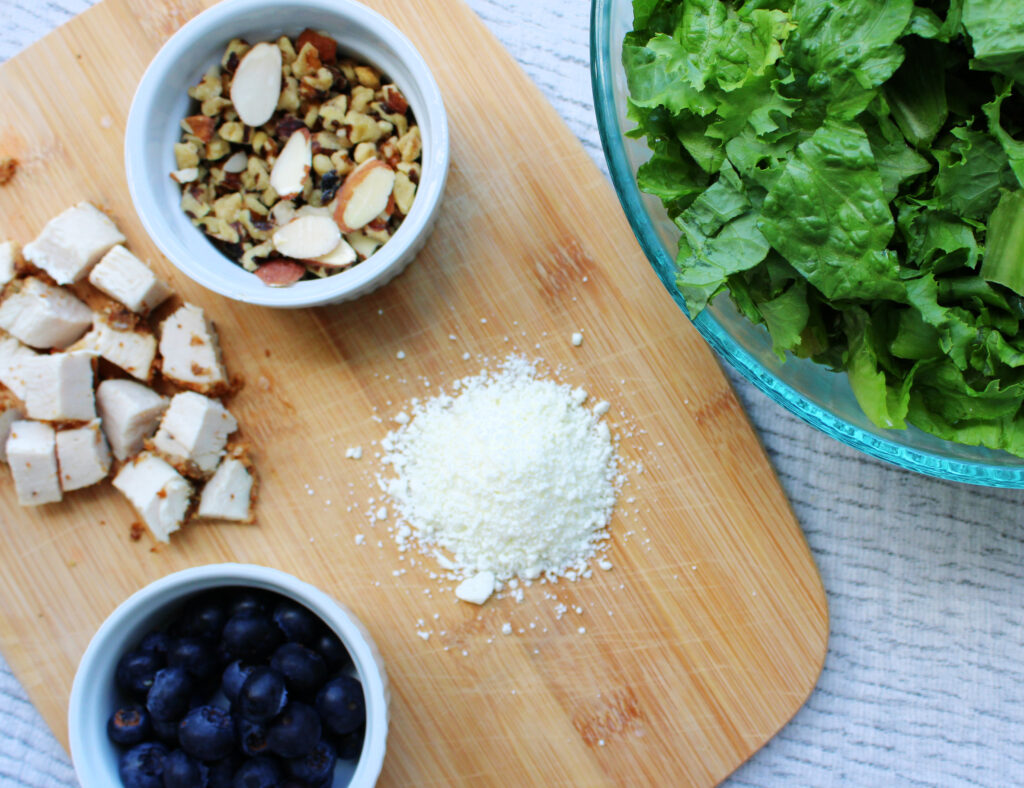 Simple Blueberry and Feta Salad with oven roasted chicken ingredients on a cutting board and lettuce in a large bowl.