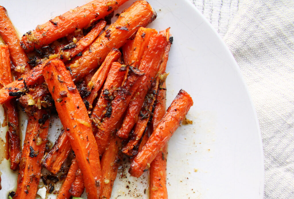 Oven roasted carrots with lemon and thyme served on a white plate.