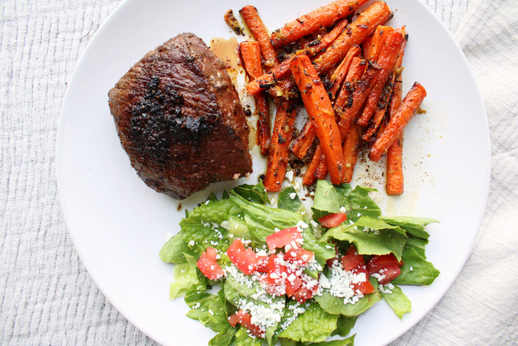 Steak, oven roasted carrots, and a salad on a white plate.