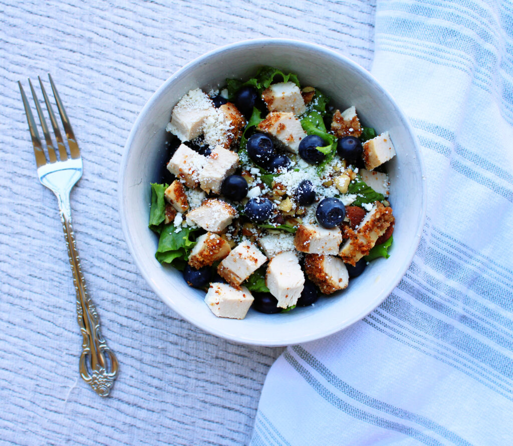 Simple Blueberry and Feta Salad with oven roasted chicken in a white bowl with fork on the left and tea towel on the right.