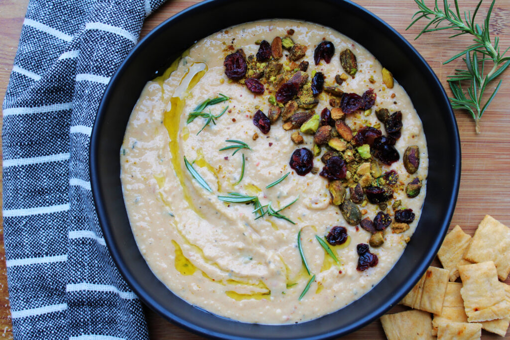 Spicy white bean dip on a cutting board with rosemary and crackers.
