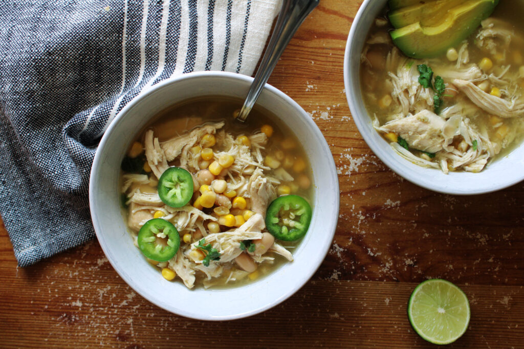 Slow cooker white chicken chili in white bowls next to a tea towel.