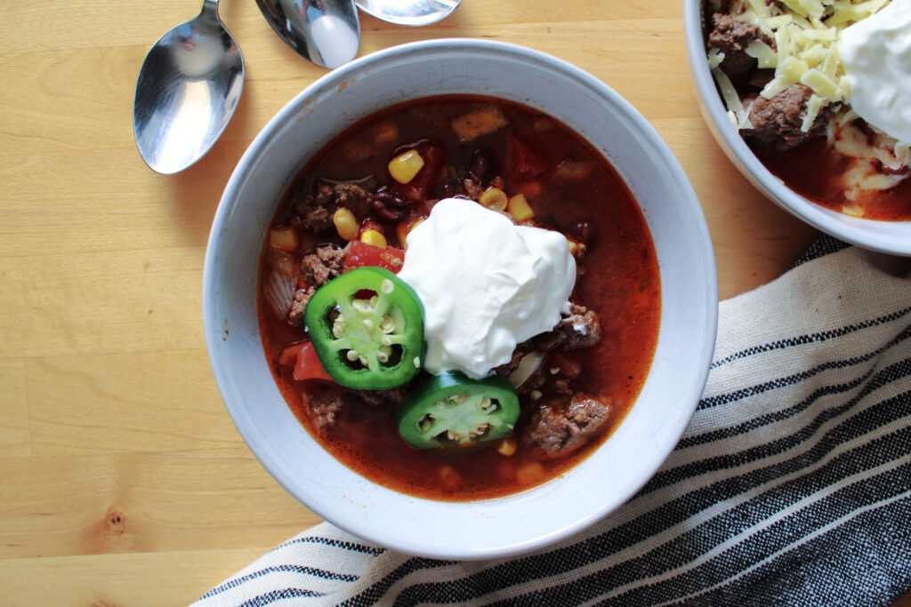Slow cooker cowboy chili with spoons and tea towels on a table.