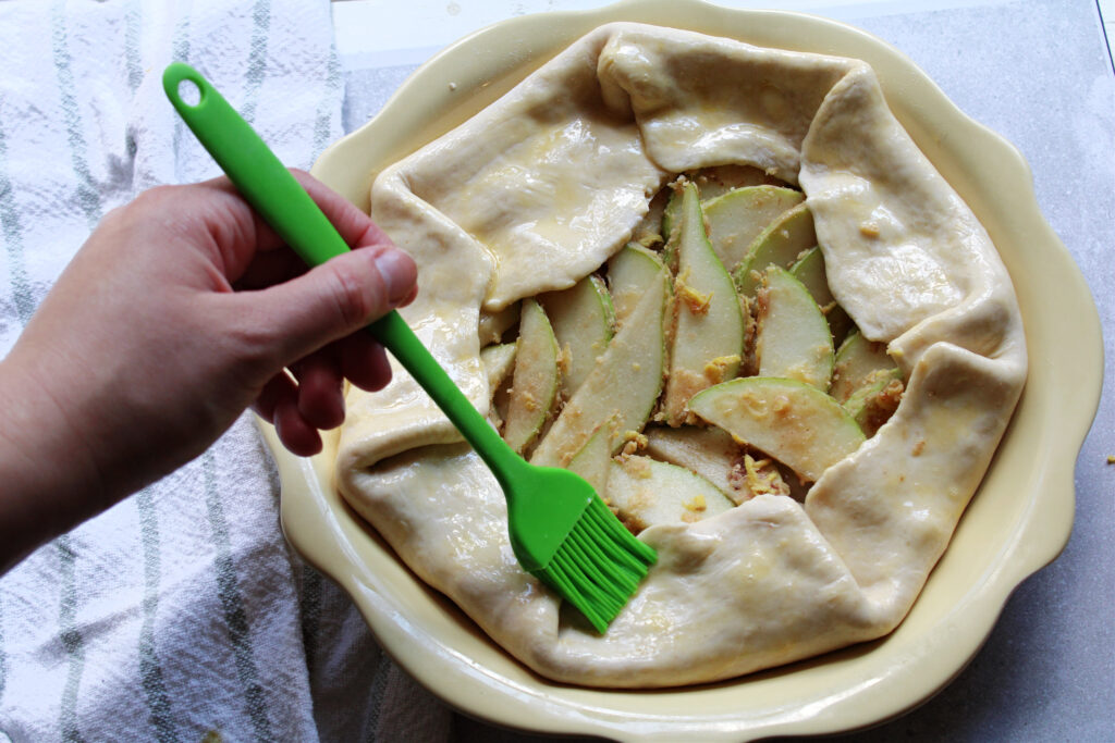 Shot of pear and ginger galette pie crust being brushed with egg wash.