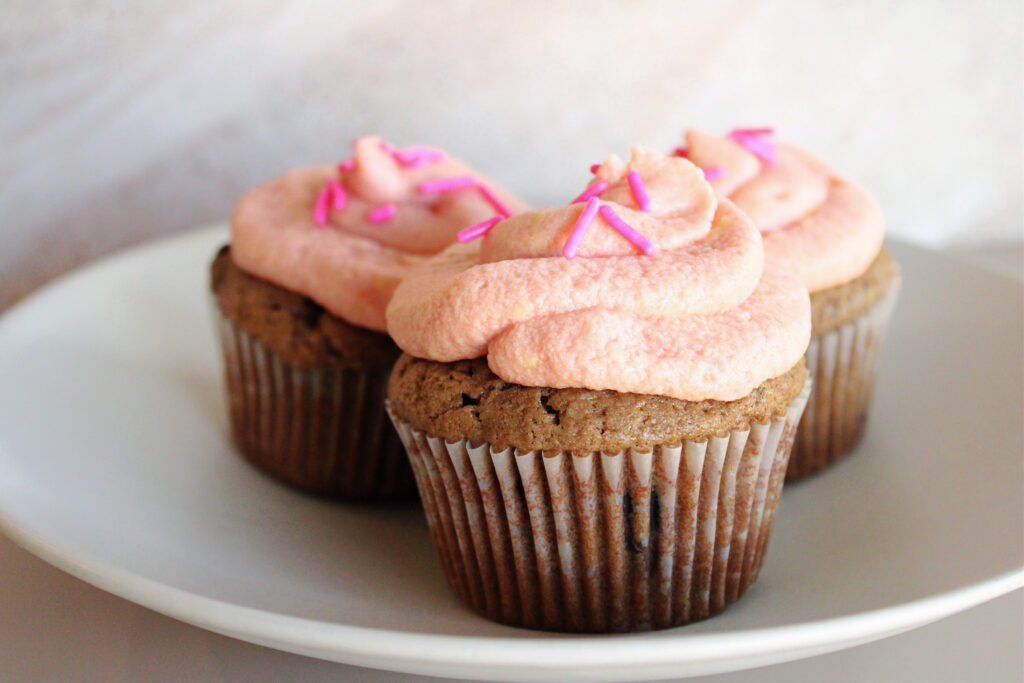 Chocolate chip sourdough cupcakes with pink frosting on a plate.