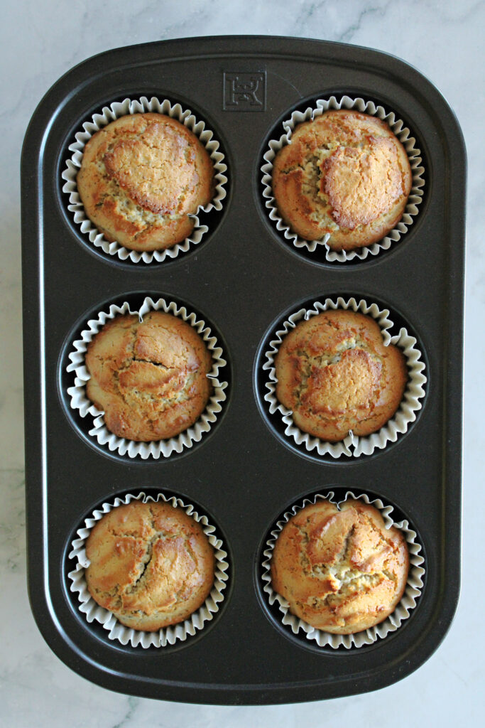 Muffins baked in a muffin tin cooling on the counter.