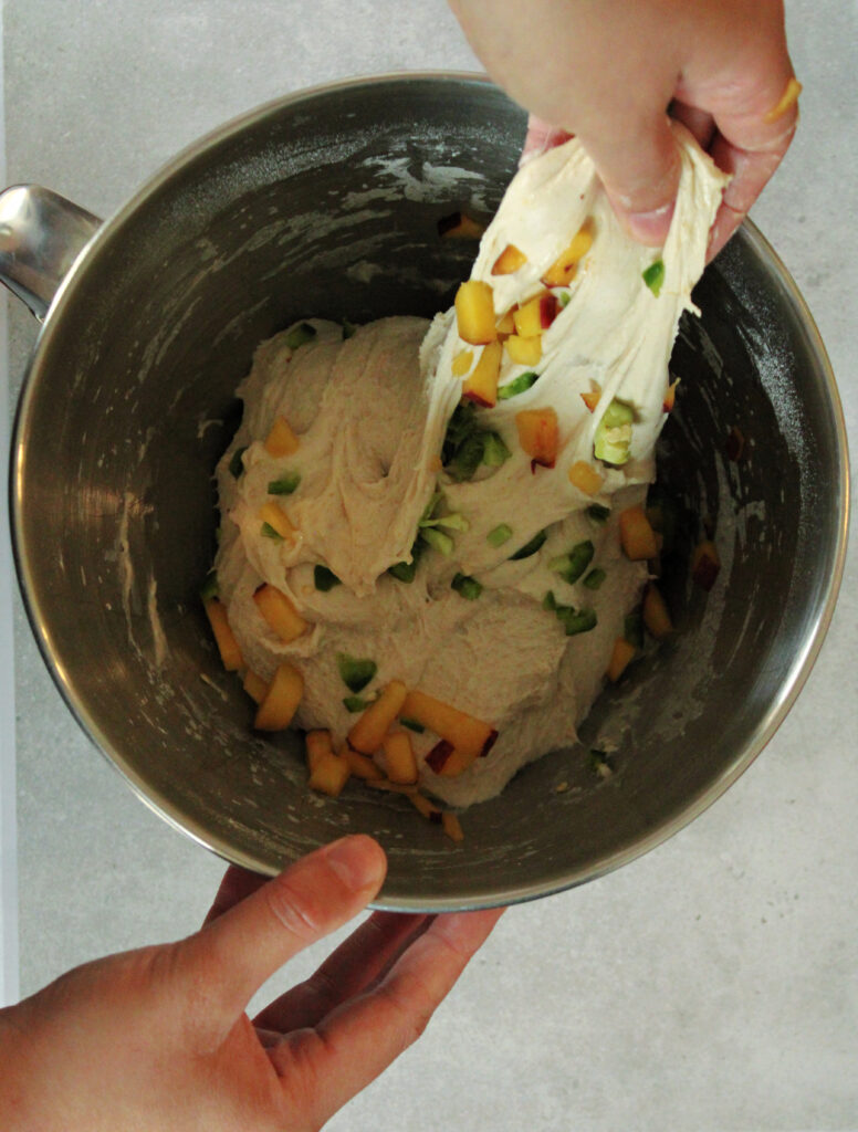folding jalapenos and peaches into sourdough in a mixing bowl.