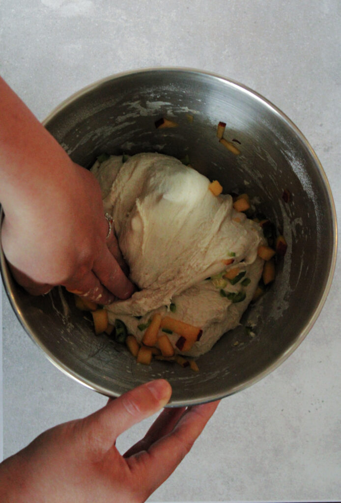 folding sourdough over jalapenos and peaches in a mixing bowl.