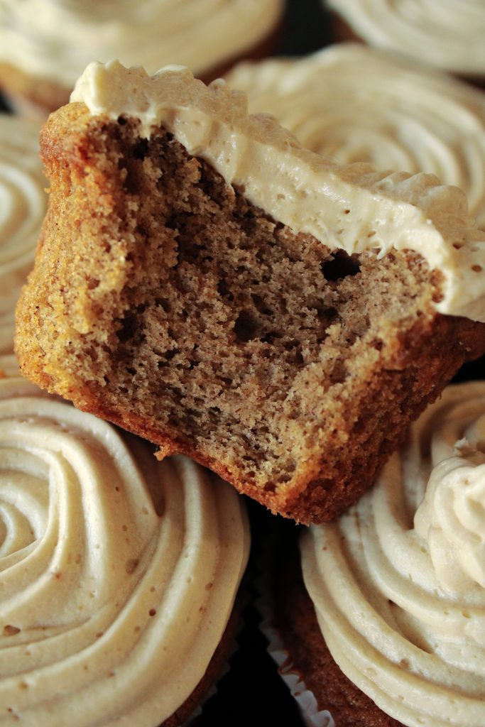 Cinnamon Cupcake with Cookie Butter Frosting bitten into sitting on top of the other cinnamon cupcakes.