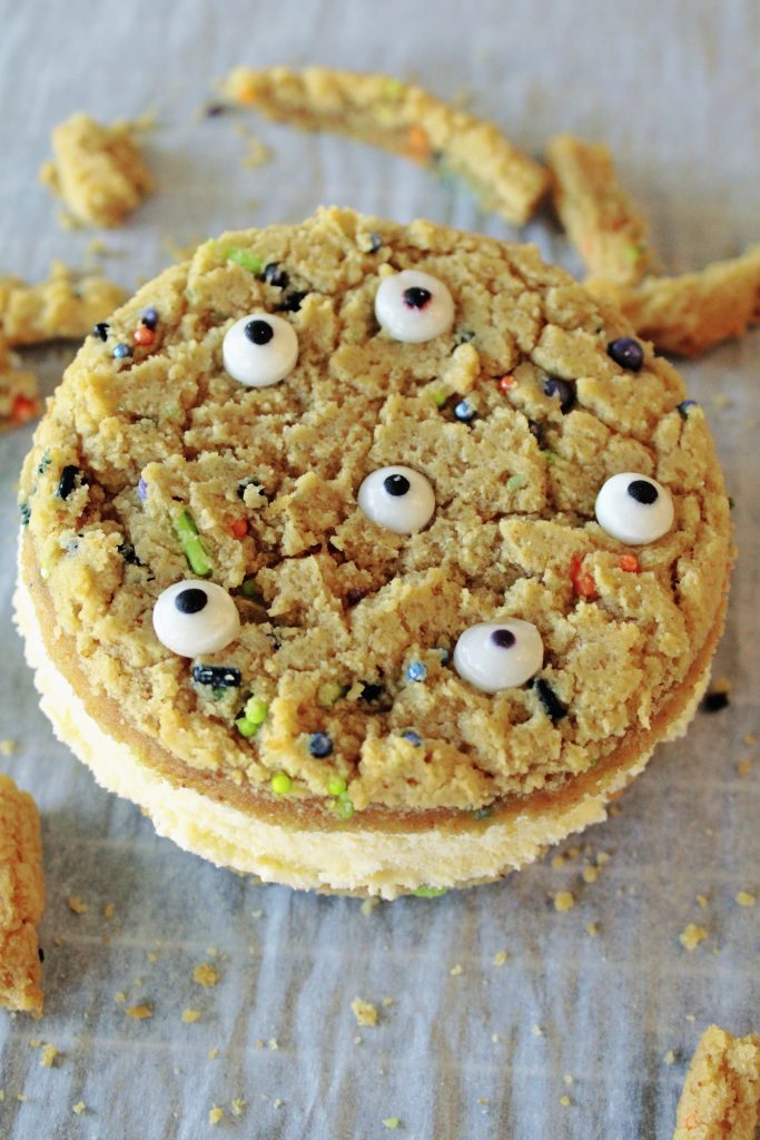 Halloween Monster Ice Cream Sandwiches sitting on parchment paper with cookie bits around it.